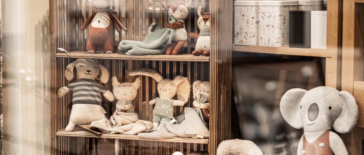 Ein helles Holzregal im Schauplatz Kevelaer mit verschiedenen Kuscheltieren wie Hasen und Rehen sowie Teedosen in sanften Farben.