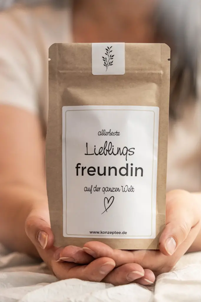 Hände halten eine Teetüte von KonzepTEE mit der Aufschrift „allerbeste Lieblingsfreundin auf der ganzen Welt“.