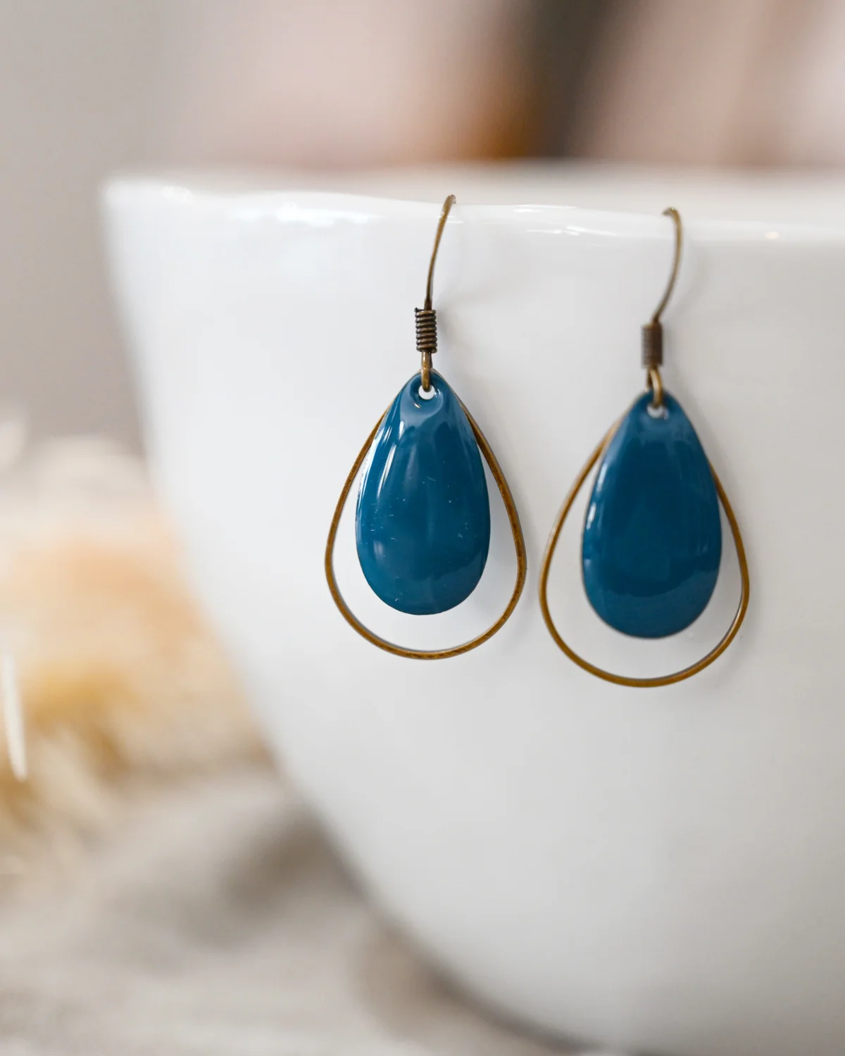 Paar Ohrringe mit blauen, tropfenförmigen Anhängern und goldfarbenen Metallfassungen.